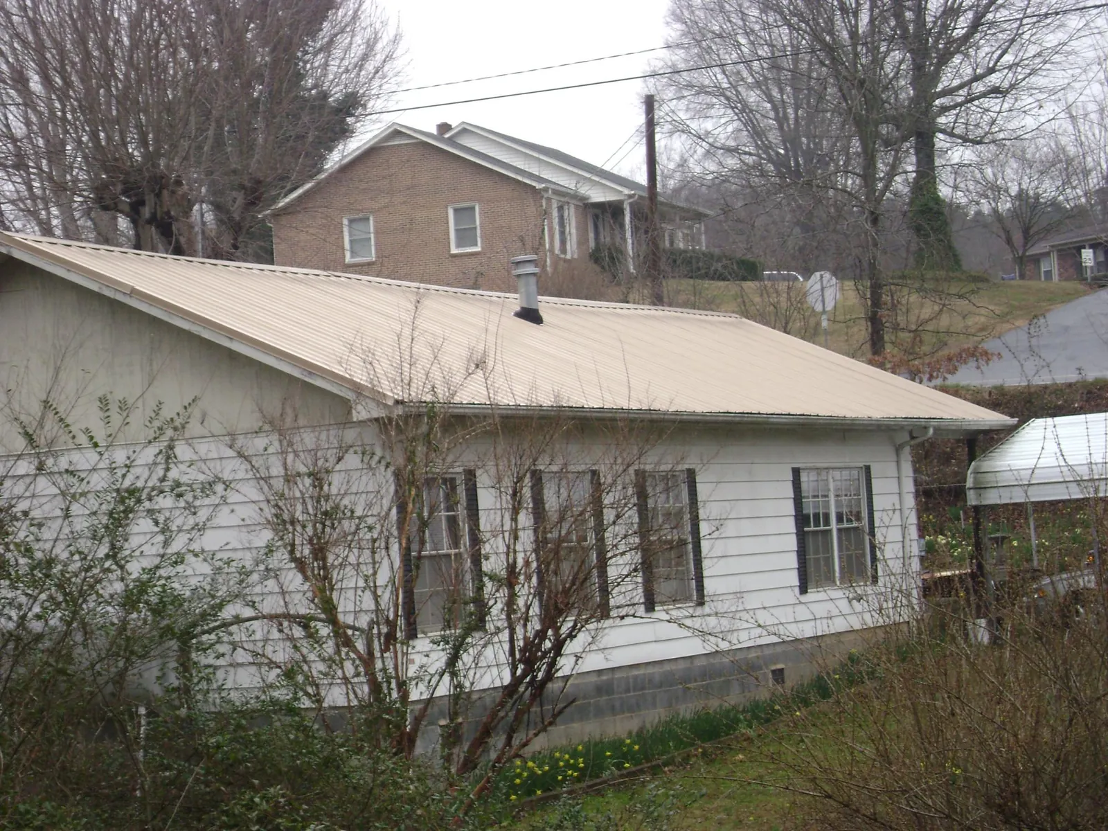 Tan metal roof on a white sided house set into a hillside — Commercial Roofing by Roofing Brothers in Victor